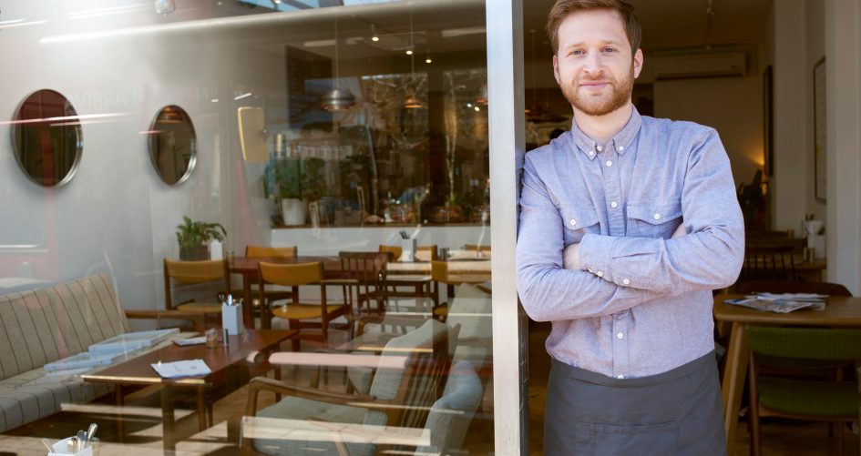 Portrait of young male cafe owner with arms folded in doorway